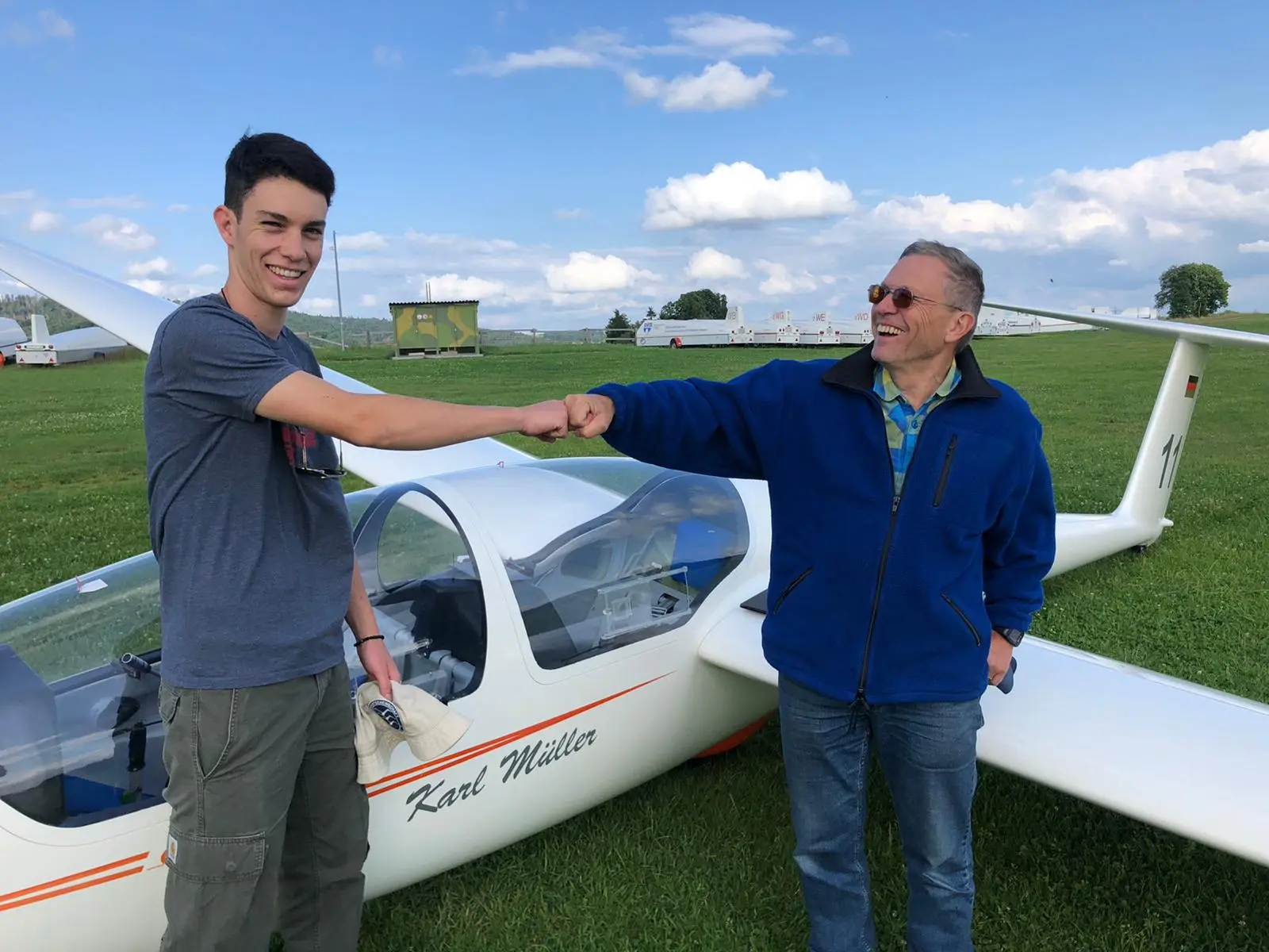 Fluglehrer und Flugschüler geben sich einen Faustgruß vor einem Doppelsitzer