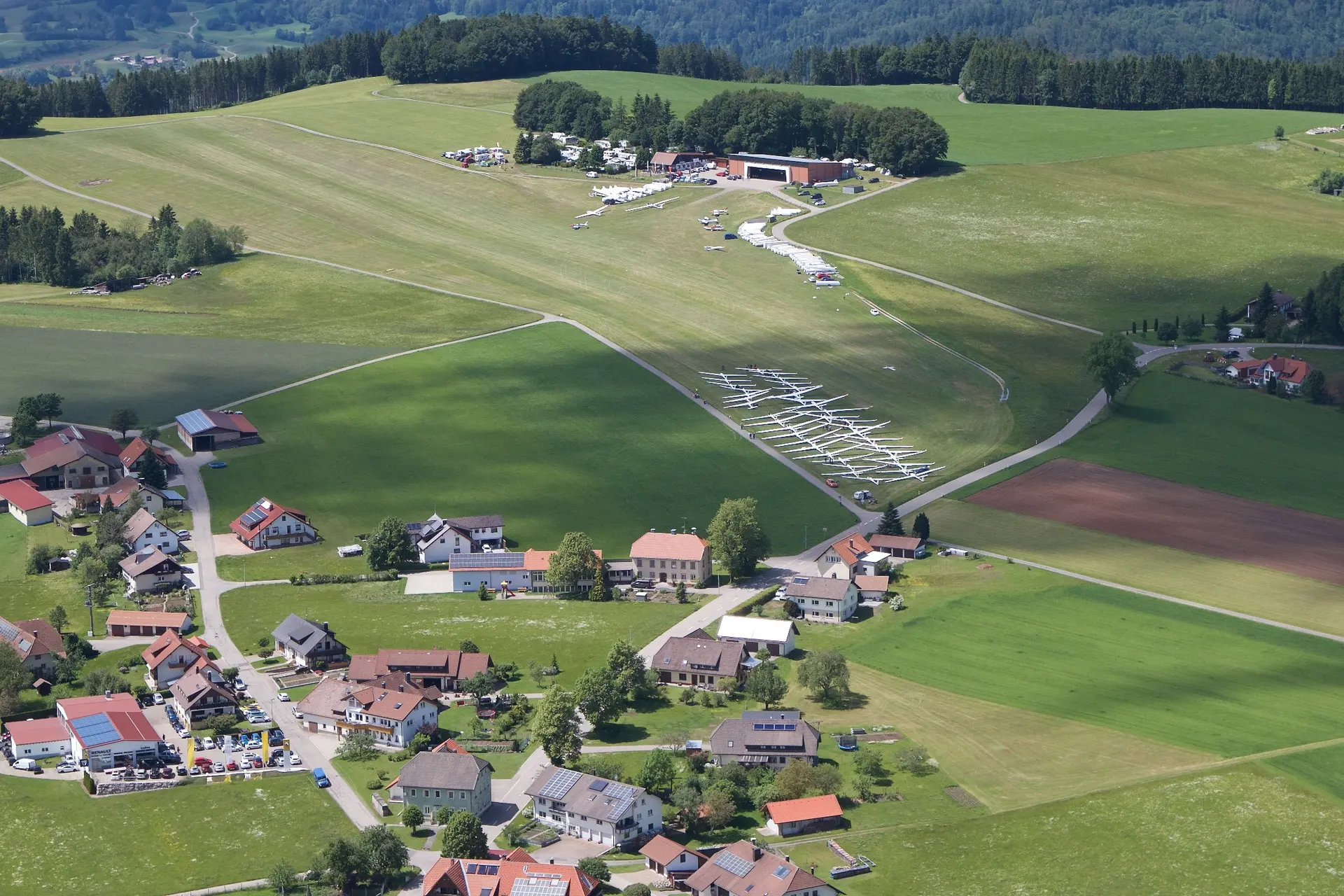 Luftbild des Flugplatzes mit Hangar, Camping und über zwanzig aufgereihten Segelflugzeugen
